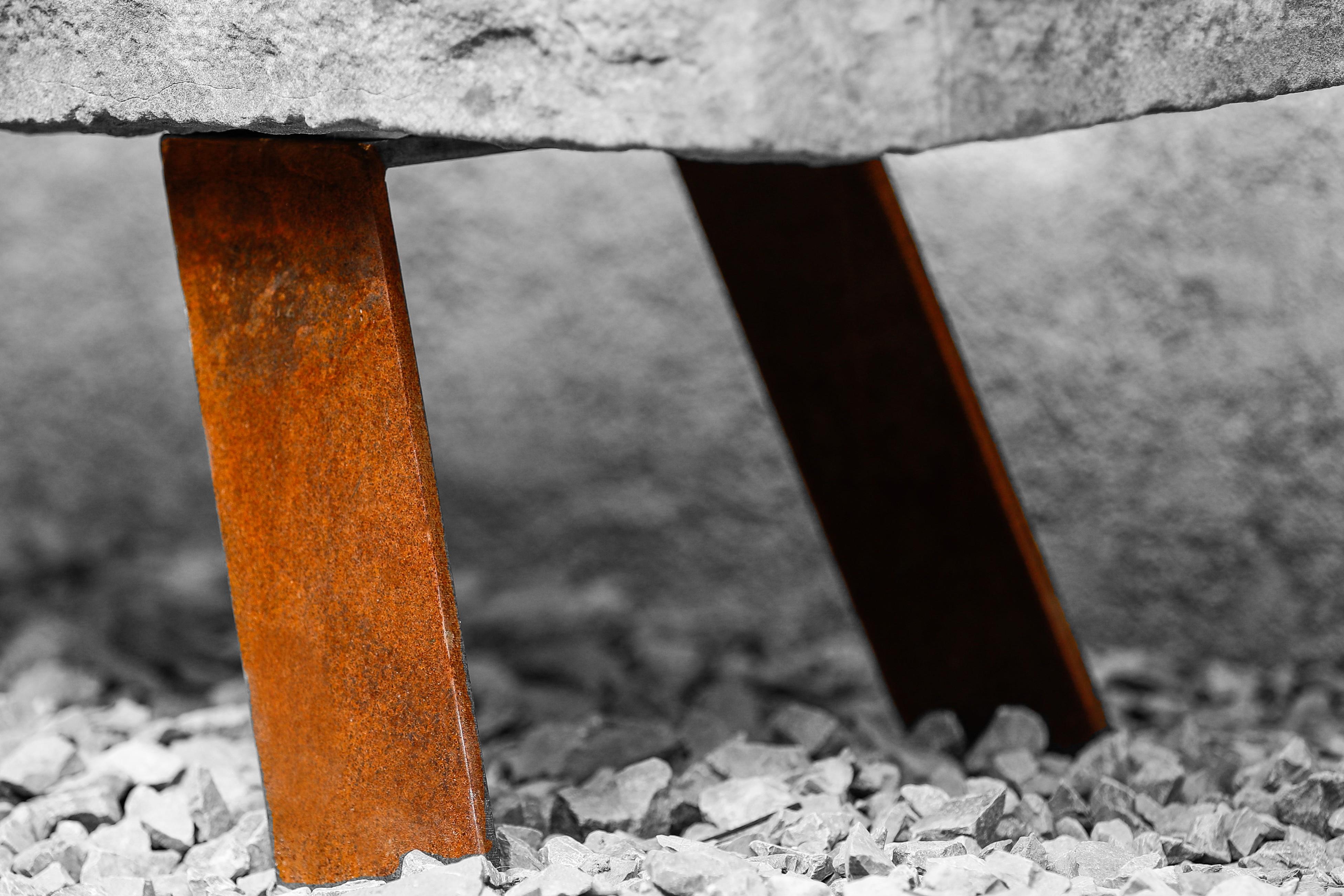 Corten steel legs supporting natural stone bench — patina detail on gravel